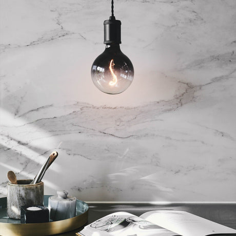 Colors Soft LED G125 3-Step Bulb in smoke glass with visible S-shaped filament, hung from a black pendant fitting against a marble wall.
