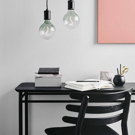 Two Colors Soft LED G125 pendant bulbs with green gradient glass and S-shaped filament, hanging above a black desk in a home office setting.