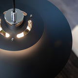 Close-up of the Sørup Pendant Light 40cm in matte black metal, showing the chrome mounting cylinder and cut-out vents that reveal glowing bulb light beneath the shade.