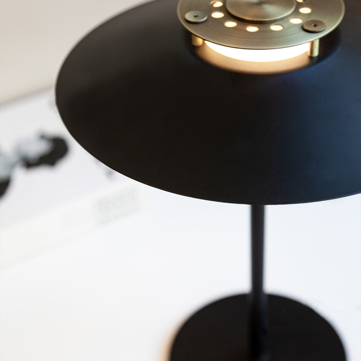 Rivoli Table Lamp 24cm close-up in black and copper, showing the wide flat black shade, lit opal glass drum, and perforated copper cap on a black stem base.