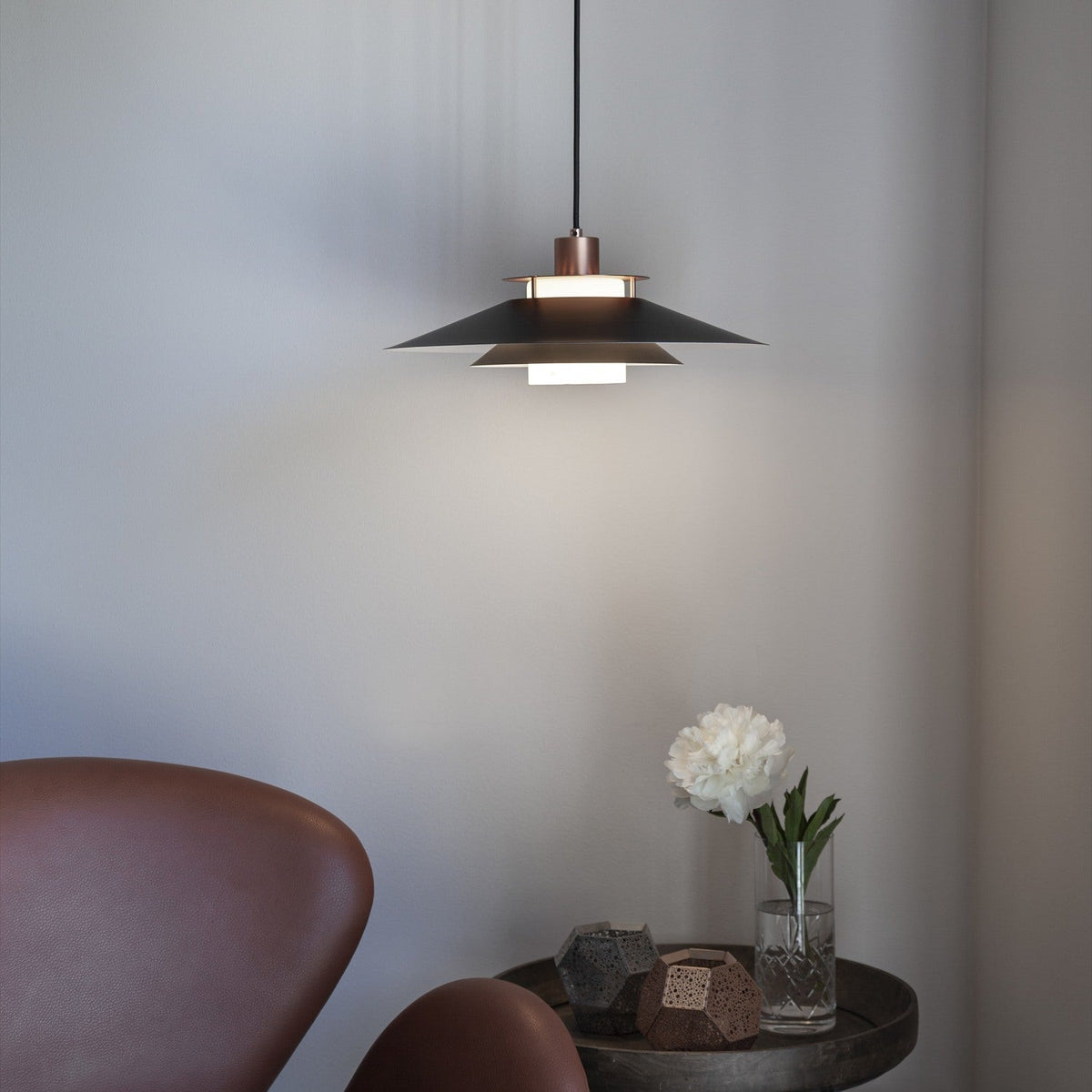 Rivoli Pendant Light 40cm in black and copper, a flat tiered metal shade with stacked copper rings, hanging above a side table in a living room setting.