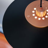 Close-up of the Rivoli Pendant Light 40cm in black and copper, showing the copper diffuser ring with circular cut-outs illuminated around a central cylinder beneath the flat black shade.