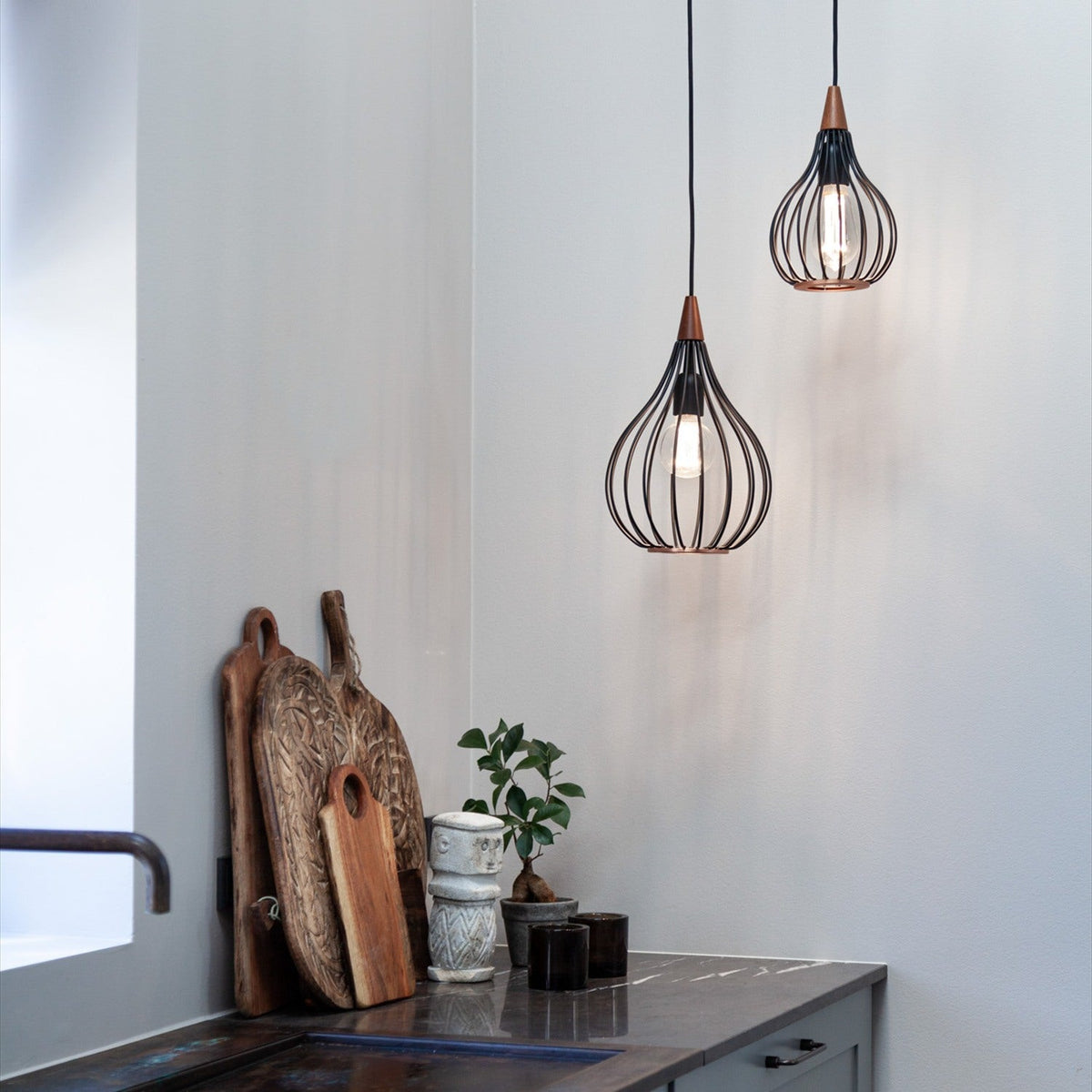 Drops Pendant Light 30cm in black wire teardrop-shaped cage with dark wood cap, shown with a second unit in a kitchen setting above a wooden countertop.