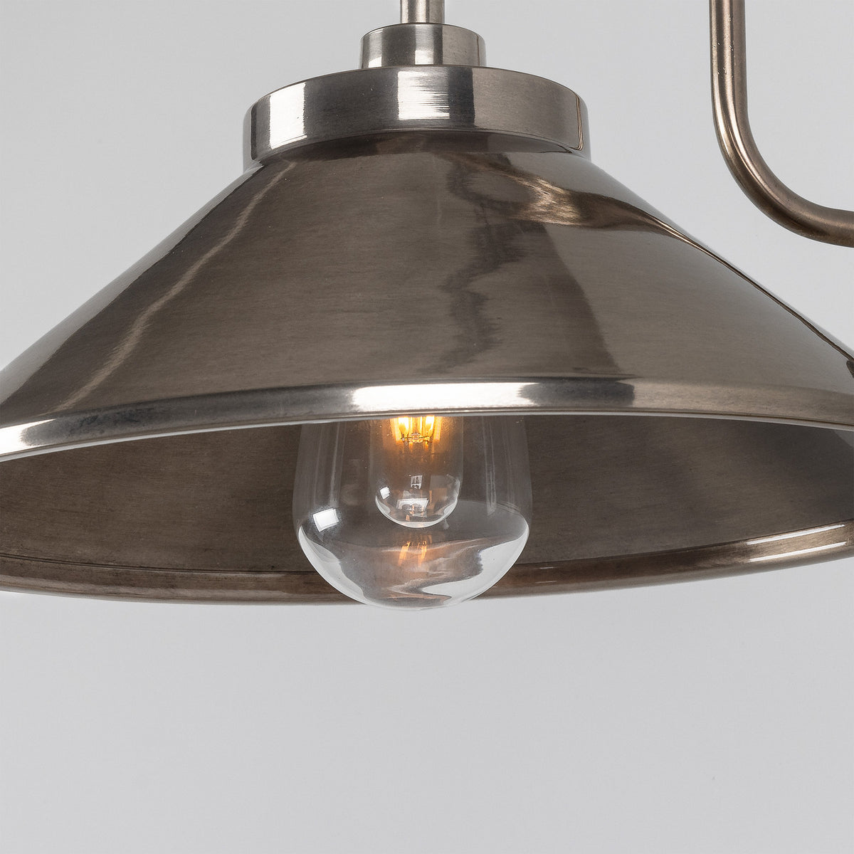 Close-up of the Halvery Brass Swan Neck Wall Light's cone shade in a dark metal finish with a visible bulb, set against a plain grey background.