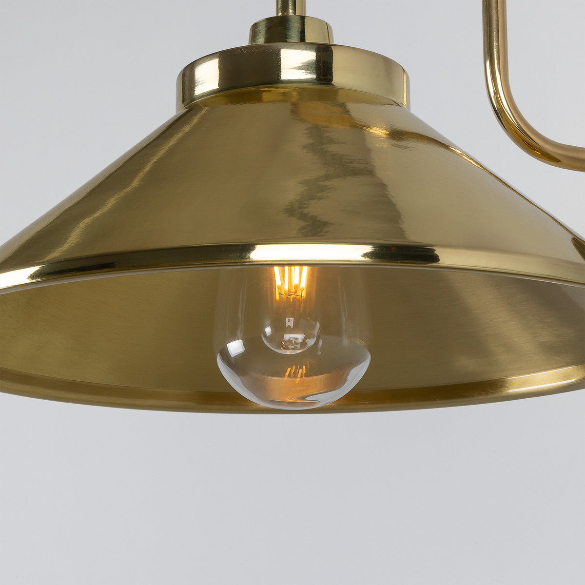 Close-up of the Halvery Brass Swan Neck Wall Light IP65, showing a wide cone metal shade in polished brass with a glowing E27 bulb visible beneath, set against a plain light background.
