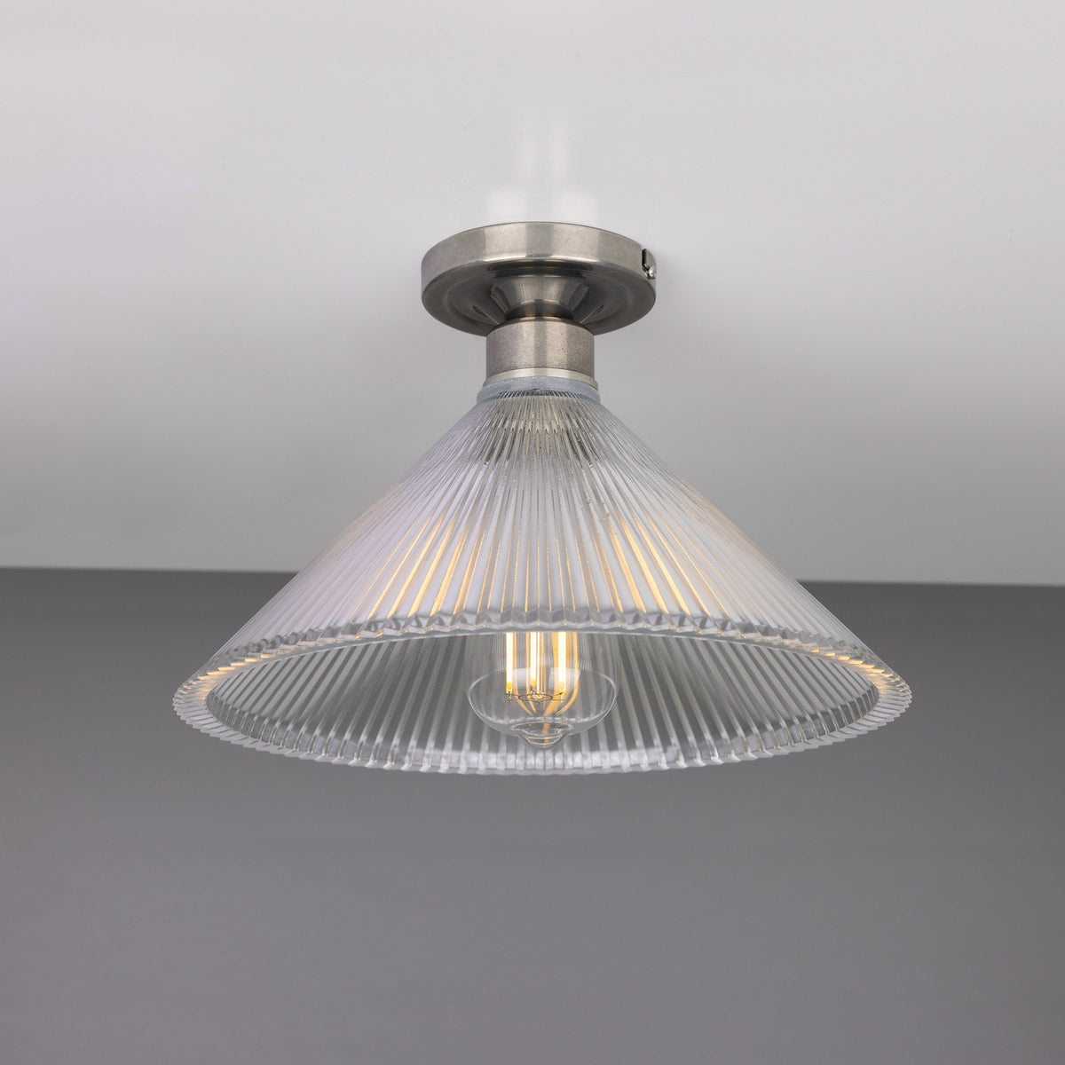 Hanoi Ribbed Glass Flush Ceiling Light with a cone-shaped prismatic glass shade and silver ceiling plate, shown lit against a plain grey background.