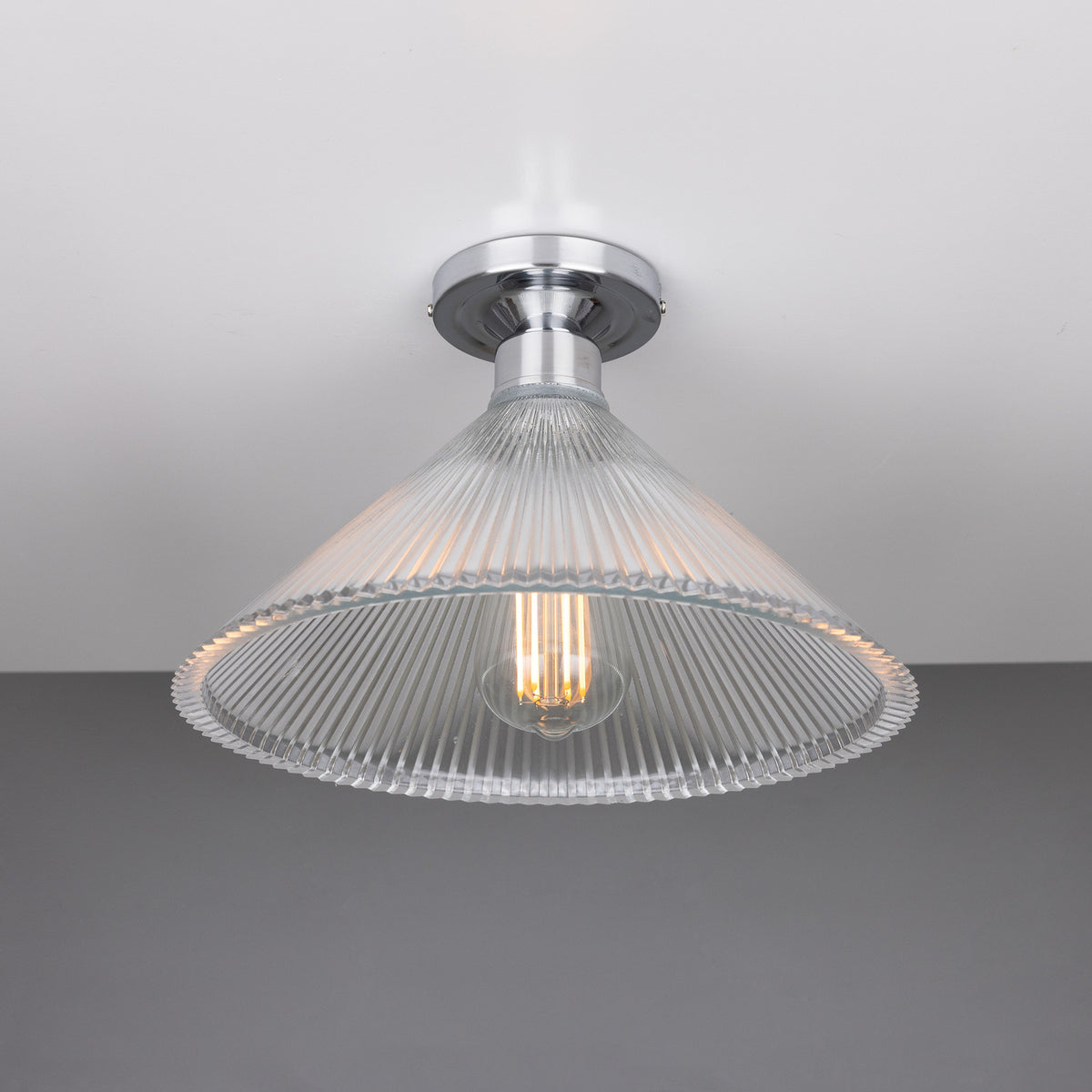 Hanoi Ribbed Glass Flush Ceiling Light with a cone-shaped clear ribbed glass shade and chrome ceiling plate, lit by one exposed E27 bulb against a plain background.