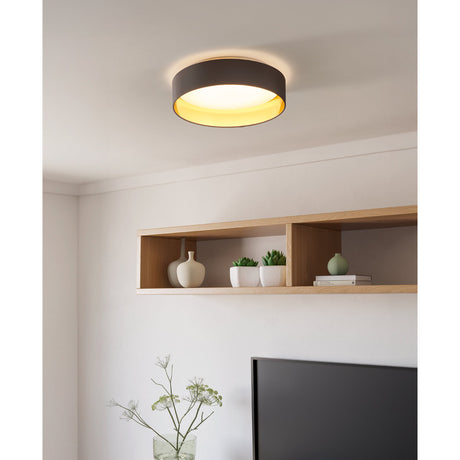 Hasanne LED flush ceiling light in mocha fabric with gold lining and white diffuser, shown fitted above a wall-mounted shelf in a living room setting.