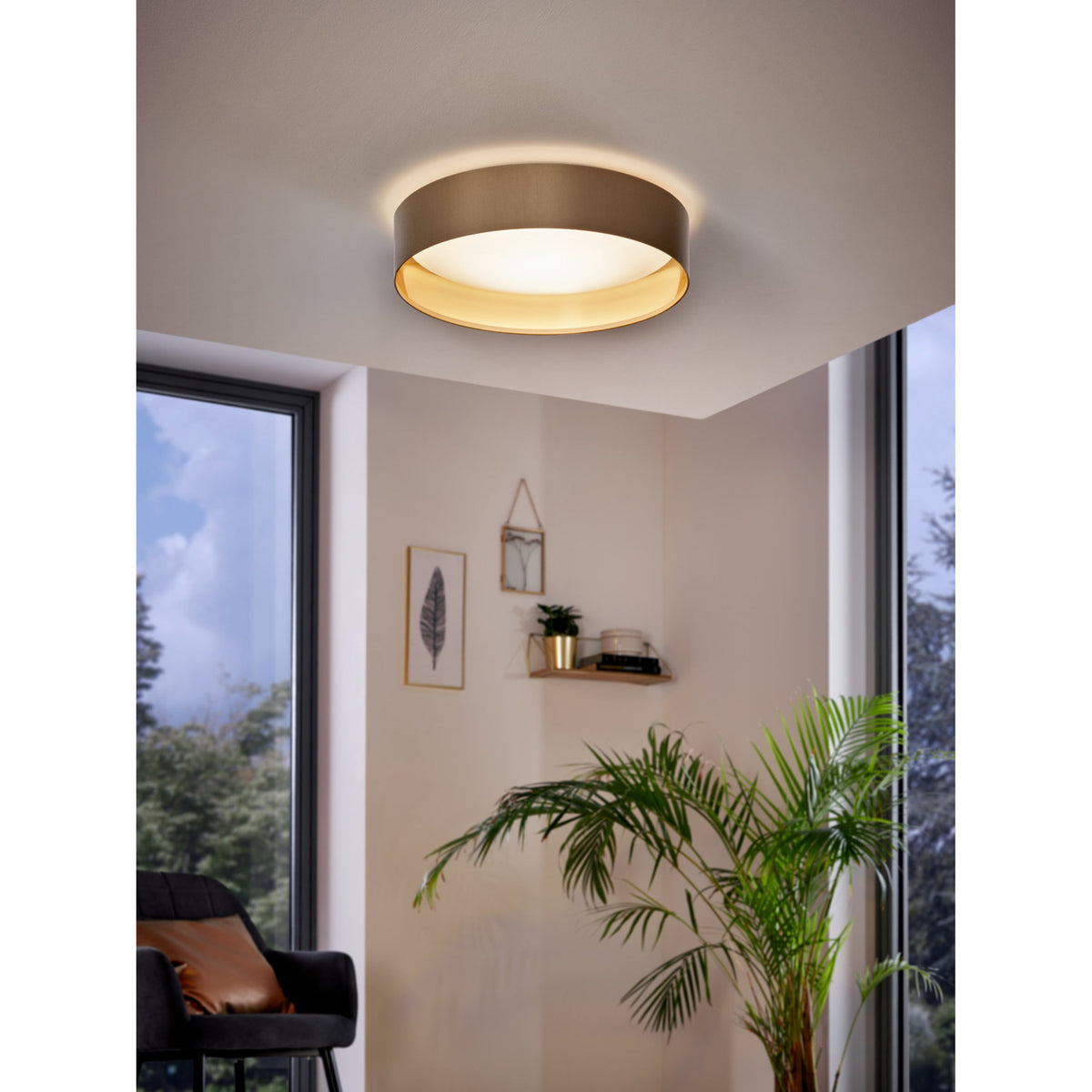 Hasanne LED flush ceiling light with round taupe fabric shade and gold lining, warm white glow, installed on a corner ceiling above a living room with plants and artwork.