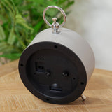 Rear view of the Bee Alarm Mantel Clock in grey metal, showing the chrome ring handle, snooze and time-set dials, and angled rear legs on a wooden surface.