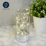 Cylindrical glass tube LED light-up decoration, 20cm, with warm fairy lights and silver beads on a mirrored silver base, shown on a marble surface beside a potted plant.