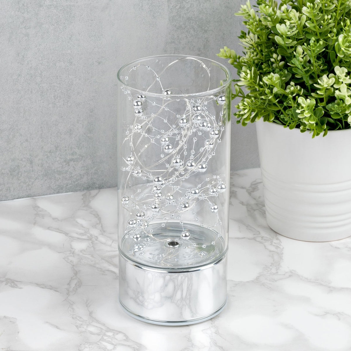 Beaded Wire Glass Tube LED Light-Up Decoration, 20cm, with silver beads on a mirrored silver base, displayed on a marble surface beside a potted plant.