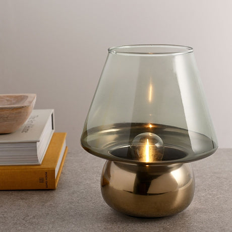 Mushroom Battery Operated LED Table Lamp 22cm in Green & Gold, with a tinted conical glass shade on a rounded gold base, shown lit on a grey surface beside books and a wooden bowl.