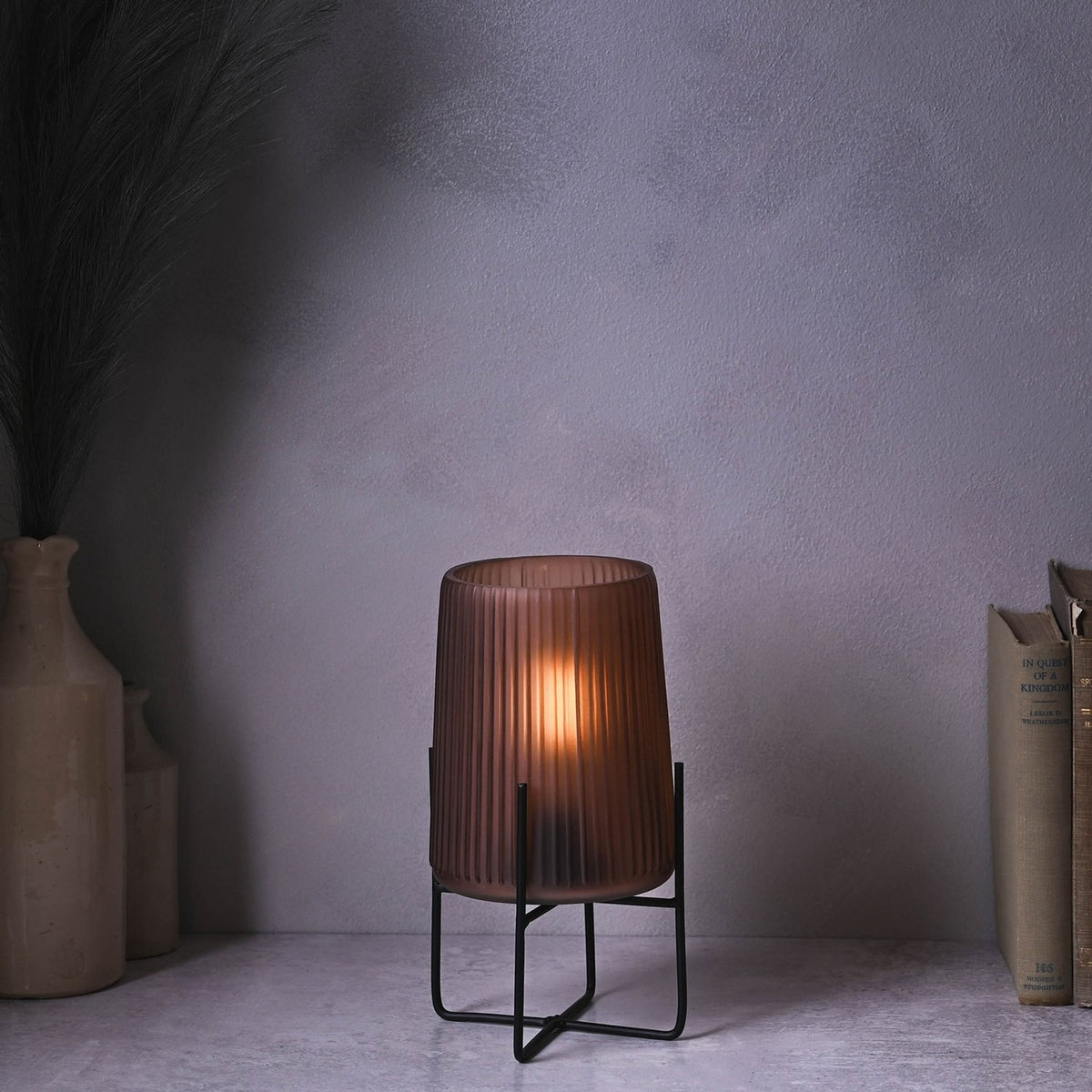 Frosted brown glass table lamp, 23cm, with ribbed vertical lines on a slim black stand, lit on a tabletop beside books and vases.