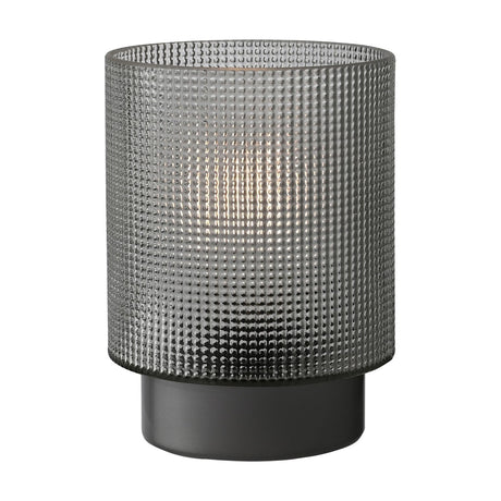 Battery operated table lamp with a cylindrical smoked grey textured glass shade featuring raised dots, set on a matte grey base, shown lit against a plain white background.