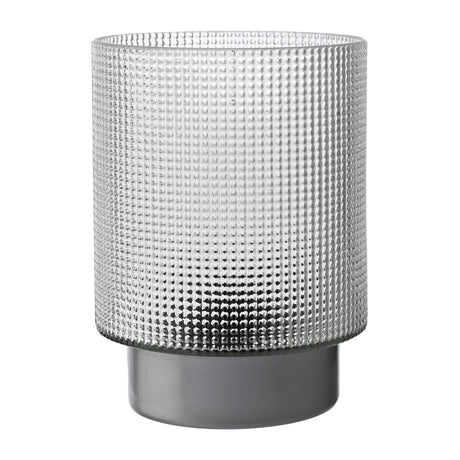 Battery operated table lamp with a cylindrical textured glass shade in smoked grey, raised dot pattern, set on a smooth grey base, shown on a plain white background.