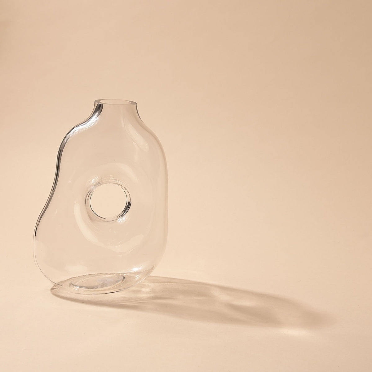 Abstract Handmade Glass Vase with Circular Hole in clear glass, showing a softly rounded, uneven body with a round cut-through centre, set against a plain light background.