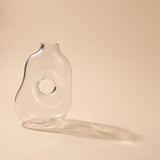 Abstract Handmade Glass Vase with Circular Hole in clear glass, showing a softly rounded, uneven body with a round cut-through centre, set against a plain light background.