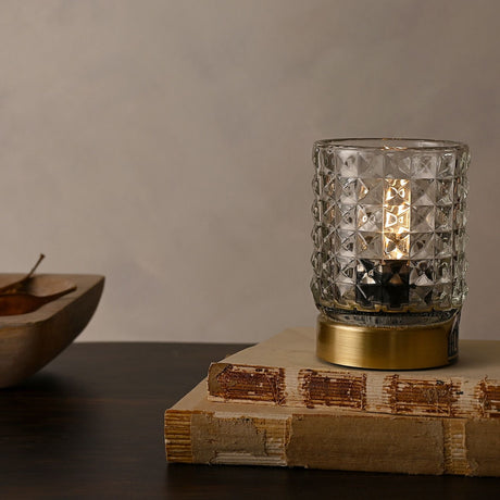 Glass Cup Table Lamp with LED Bulb, clear faceted diamond-patterned glass shade on a round gold base, lit on a book beside a wooden bowl.