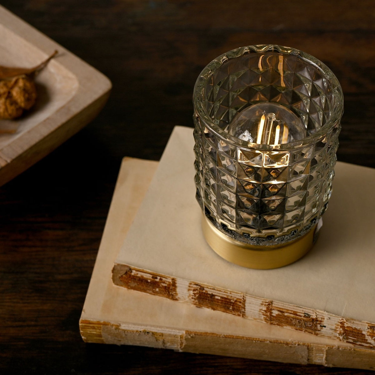 Glass Cup Table Lamp with LED bulb lit inside, faceted diamond-pattern glass shade on a round gold base, shown on a book beside a wooden tray.