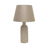 Slim ribbed bottle ceramic table lamp in beige with a weathered, flecked finish and tapered fabric shade, shown on a plain white background.