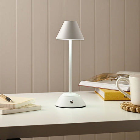 Tapered Shade Matt USB LED Touch Table Lamp, 29cm, in white with a slim stem and rounded base, shown lit on a desk beside books and a mug.