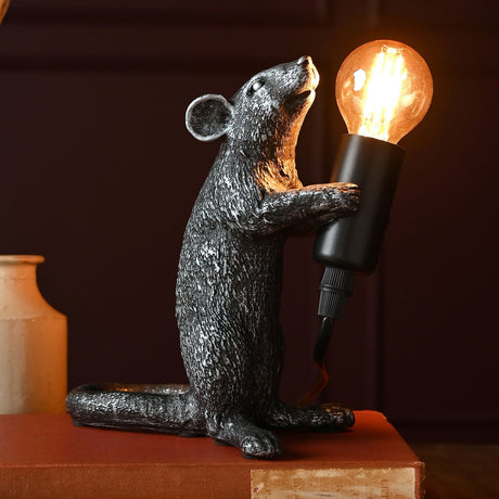 Standing Mouse Table Lamp in black resin, 18cm, holding a black bulb holder with exposed filament bulb, textured fur and curled tail, shown on a book against a dark background.