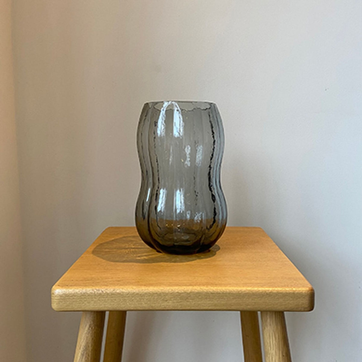 Hourglass Ribbed Textured Tall Glass Vase in smoky grey with vertical ribbing, shown on a wooden stool against a plain light background.