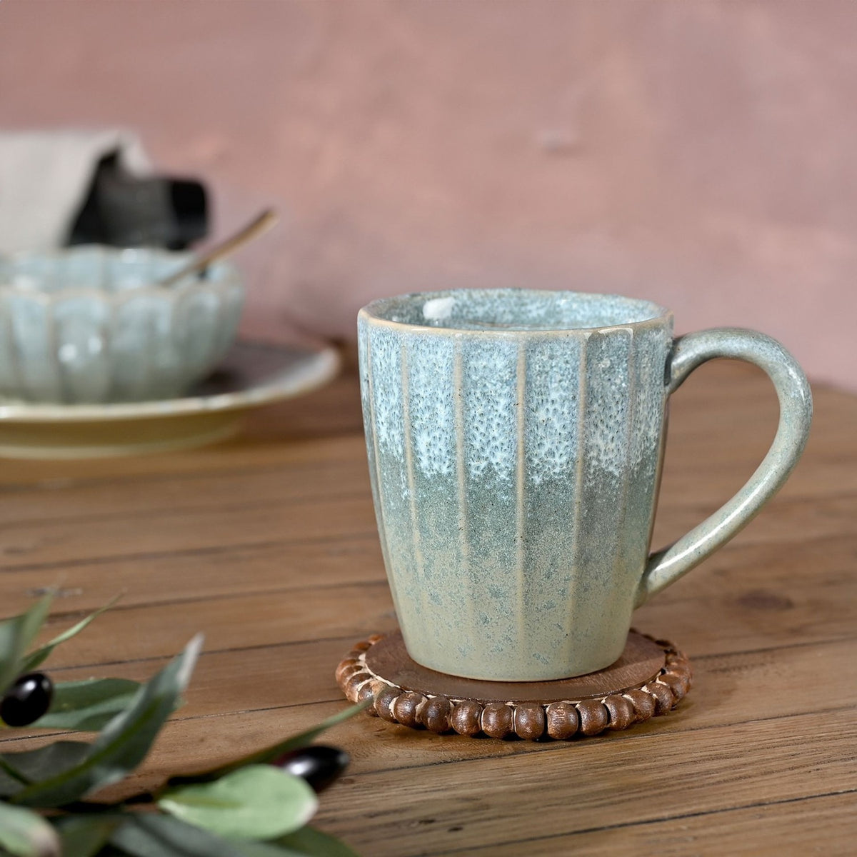 Tapered fluted stoneware mug with a speckled green glaze, lighter near the rim and deepening to grey-green at the base, shown with a ceramic handle on a wooden table.