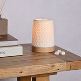 Tapered Embossed Star Aroma Ceramic Table Lamp, 15cm, in white with a star-patterned perforated design, on a round wooden base, shown lit on a wooden table beside wax melts and books.