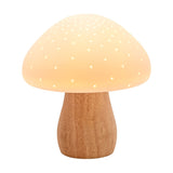 Pierced mushroom ceramic table lamp with a glowing white, pin-pricked cap and curved natural wood-tone stem base, shown lit against a plain white background.