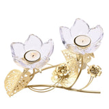 Two-stem flower candle holder with clear glass petal cups holding tealights on gold stems, accented by pierced gold leaves and small blossoms, shown on a plain white background.
