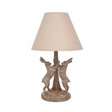 Table lamp with a wood-effect base of two hares facing each other beside a tree trunk, in brown with paler highlights, topped by a natural cone-shaped fabric shade, shown on a plain white background.