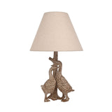Table lamp with base of two sculpted geese beside a tree-trunk stem, brown wood-effect resin finish, topped with a tapered beige fabric shade, on a white background.