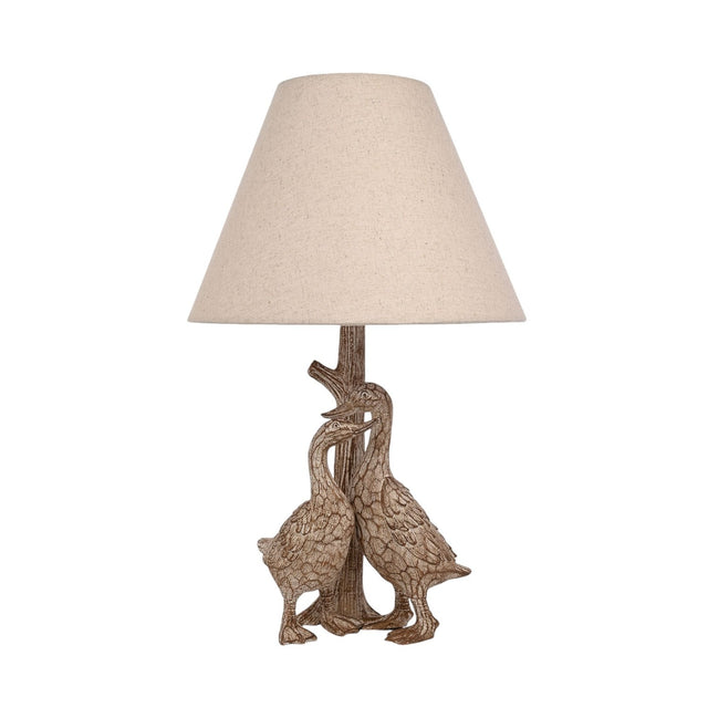 Table lamp with base of two sculpted geese beside a tree-trunk stem, brown wood-effect resin finish, topped with a tapered beige fabric shade, on a white background.