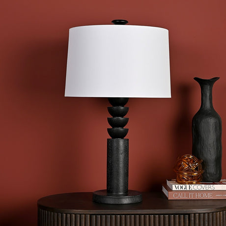 Tiered Resin Table Lamp with white drum shade and black sculptural column base, 65cm tall, shown on a dark console table against a terracotta wall.