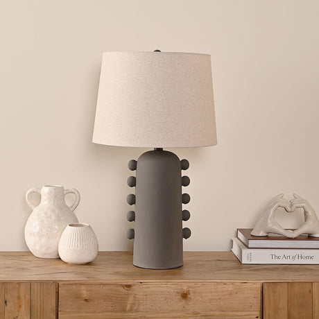 Beaded Ceramic Table Lamp with Oatmeal Shade 62cm in Grey, shown on a wooden sideboard beside ceramic vases and books in a living room setting.