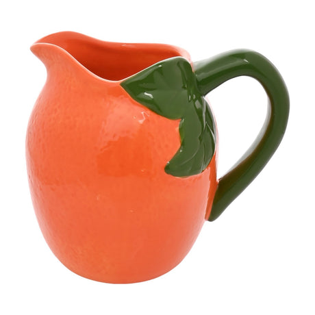 Small earthenware jug shaped like a dimpled orange, with glossy orange glaze, green leaf detail and curved green handle, pouring lip at front, on a plain white background.