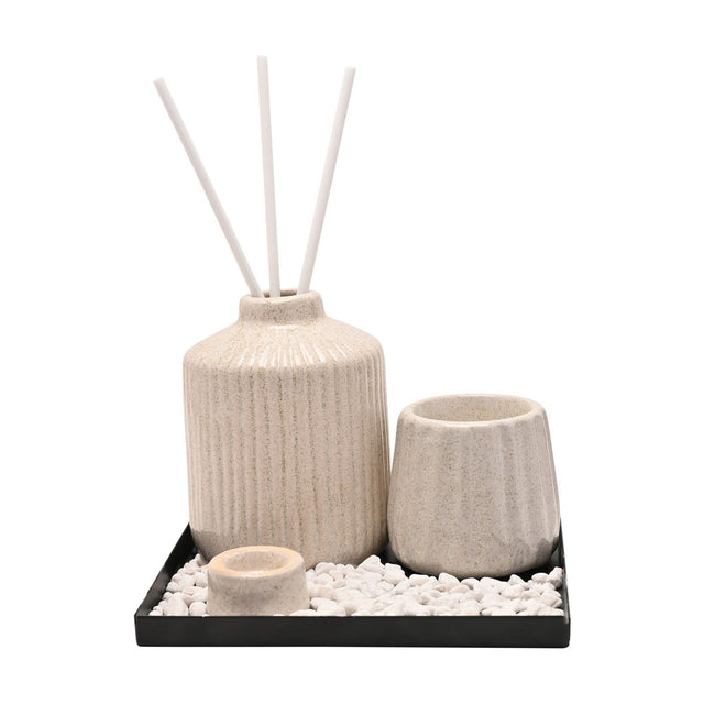 Ribbed ceramic diffuser vessel set in off-white with three white reeds, a ridged pot and small cup on a black tray with white pebbles, shown on a plain white background.