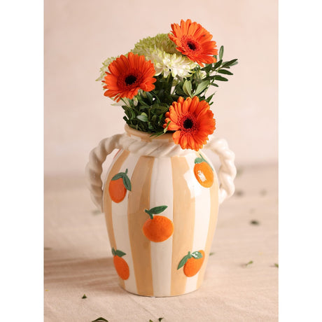 Striped ceramic vase in white and peach with raised orange and leaf details, twisted rope handles and neck band, holding orange and white flowers against a neutral background.