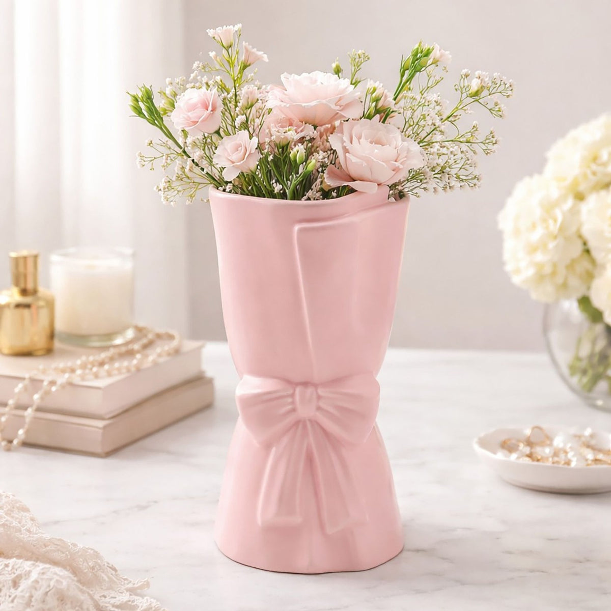 Pink ceramic vase, 24cm, shaped like a wrapped bouquet with a folded edge and ribbon bow, holding pink roses and gypsophila on a marble surface.