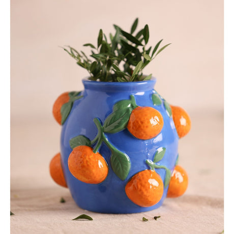 Ceramic vase, 13.9cm, blue glaze with raised orange citrus fruits and green leaves in relief, holding green foliage, against a plain light background.