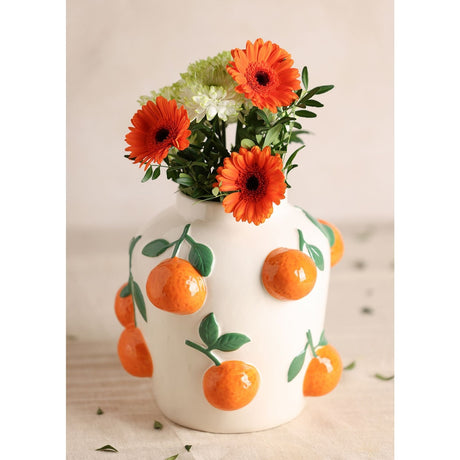White ceramic vase, 23cm, with raised glossy orange fruit and green leaf details, holding orange and white gerbera daisies, shown against a neutral background.