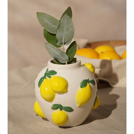 Round white ceramic vase, 12cm, with raised yellow lemons and green leaf accents in a glossy finish, shown with eucalyptus foliage against a neutral backdrop.