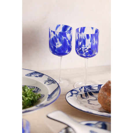 Tortoise Shell Speckled Wine Glass Set of 2 in blue and clear glass with tall rounded bowls on slim clear stems, styled on a dining table with blue and white plates.