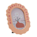 Wooden oval photo frame in pale orange with wavy edge, "Main Character Energy" in pink lettering, holding a 6 x 4in portrait photo on a white background.