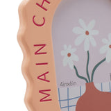 Close-up of the Main Character Energy wooden photo frame in pale orange with wavy oval edge, showing deep pink lettering and a floral 6 x 4in photo insert.
