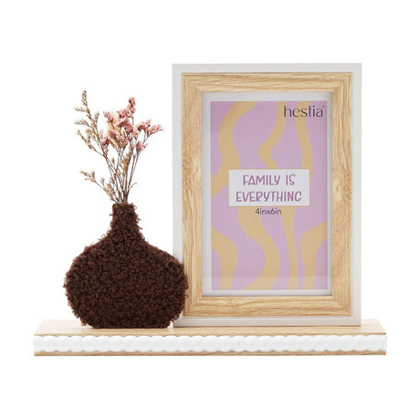 Wooden 6x4in photo frame in natural wood tone with white edge, paired with a rounded dark brown textured vase holding dried pink flowers, on a white base against a plain background.
