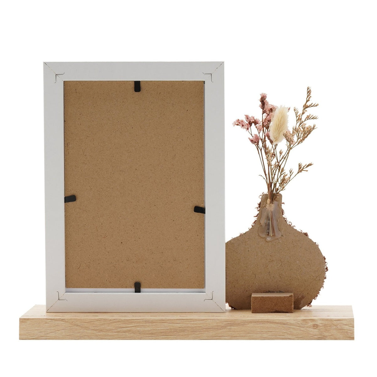 White 6x4in photo frame with wooden base, shown back-facing, beside a textured brown vase holding dried flowers, on a plain white background.