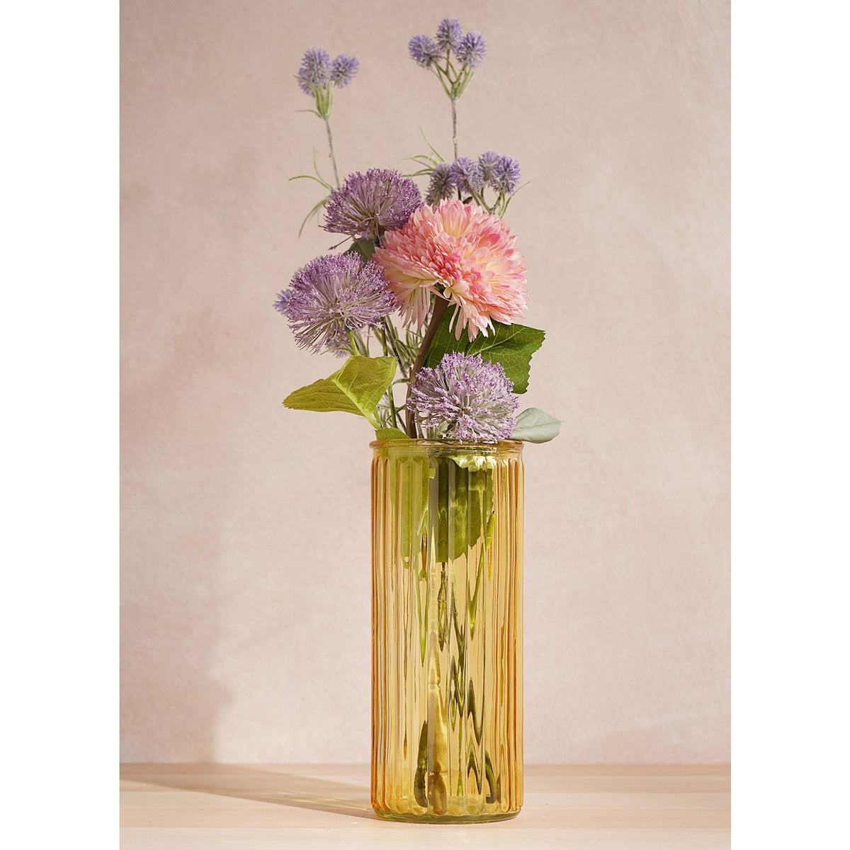 Tall Vertical Ribbed Glass Vase in yellow, slim cylindrical shape with fine vertical ribs, holding a mixed purple and pink floral arrangement against a plain light background.